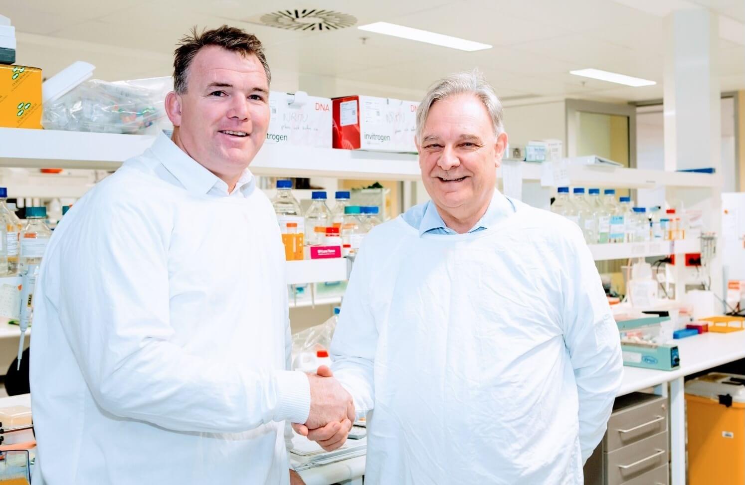 CEO and collaborator shaking hands in a lab wearing protective gowns