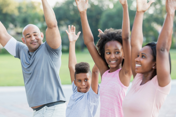 A family is outside in a park doing an exercise program together.